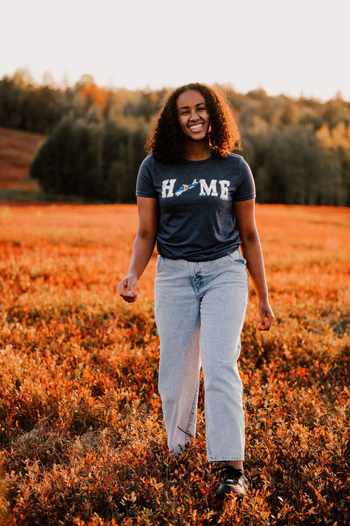 Model walks in a sunny field in autumn wearing our Nova Scotia HOME flag Unisex t-shirt. Navy haze t-shirt made and printed in Truro, Nova Scotia with the word HOME printed in large white letters across the chest. A small outline of the province of nova scotia replaced the O in home.